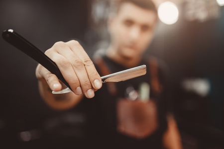 Barber shop. Close-up of barber holds razor for shaving his beardの写真素材