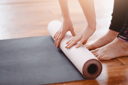 Yoga. Close-up woman folding roll fitness or yoga mat after working out home in living room. Concept healthy life. の写真素材