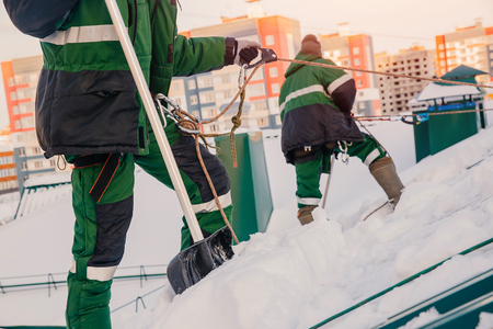 Team of male workers clean roof of building from snow with shovels in securing belts of mantra.の写真素材