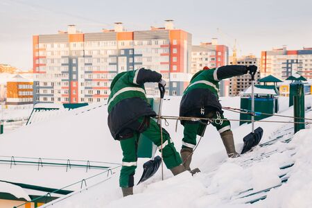 Team of male workers clean roof of building from snow with shovels in securing belts of mantra.の写真素材