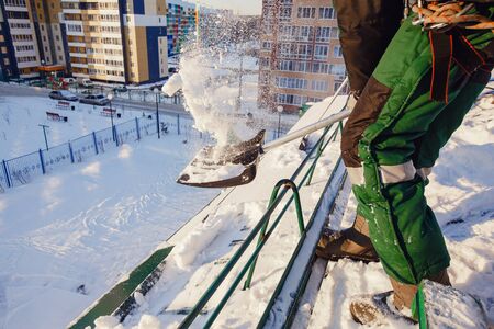 Team of male workers clean roof of building from snow with shovels in securing belts of mantra.の写真素材