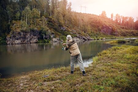 Fishing. The fisherman on a background of rocks throws the fishing rod into the water for catching fish. Concept rest, hobbyの写真素材