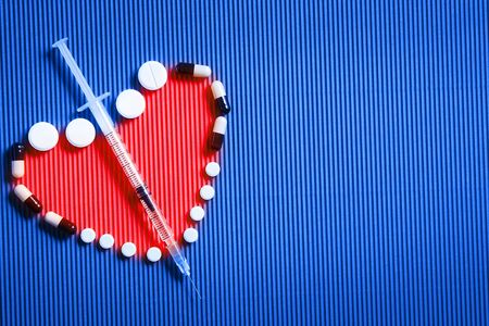 Medical preparations, pills and capsules and syringe lie on blue background in shape of heart. Copy spaceの写真素材