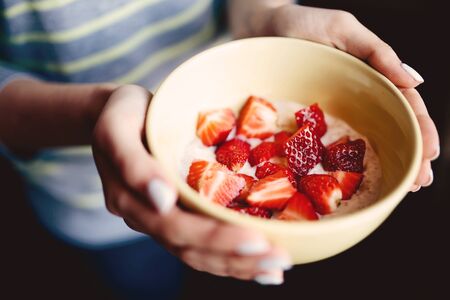 Girl is holding a cup of porridge and chopped fresh strawberries. The concept is a healthy and nutritious breakfast for athletes.の写真素材
