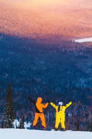 Lover couple on snowboard look mountain, sunset, concept of St. Valentineの写真素材