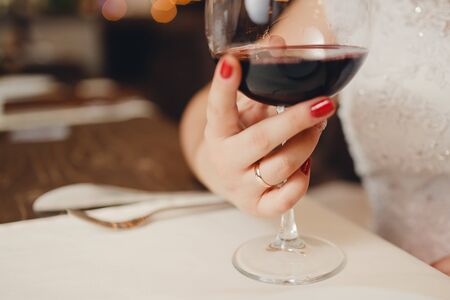 Close-up of the hand of a white girl holding a glass of wine, on the finger a wedding ring, a red maniure on her nailsの写真素材
