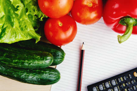 Fresh vegetables on the table: red pepper, lettuce, cucumber, tomatoes, sheet for notes - notepad. Cutting board, Food imitation. Inflationの写真素材