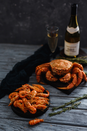 Seafood shrimp. Close-up of ready-made shrimps lie in plate, dark background. In background, crab hairy, bottle of champagne and glass. Concept grilled dinnerの写真素材