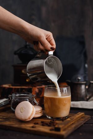 Coffee. Breakfast. Hand of girl pours milk into coffee, next to macaroni, in background coffee grinder, coffee beans, gray background,の写真素材