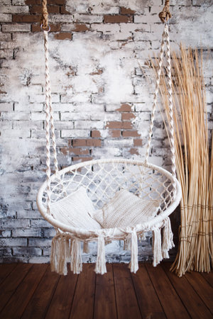 Armchair hanging. Design of a swing for the house from ropes and a rope with white pillows