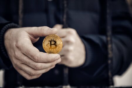 Imprisoned hacker holds coin bitcoin and prison lattice. Concept arrest, fraud and deception with crypto currency and mining.の写真素材