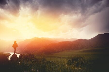Traveling woman with backpack looking river and mountains, sunny day. silhouetteの写真素材