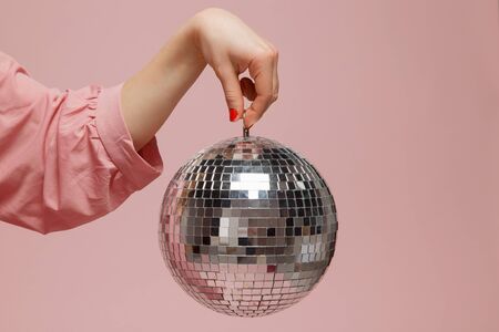 Mirror disco ball girl holding her hand on pink background. Concept party, holiday. Copy spaceの写真素材