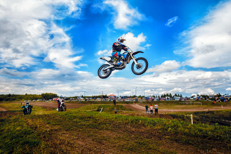 Racer on motorcycle dirtbike motocross cross-country in flight, jumps and takes off on springboard against sky.の写真素材