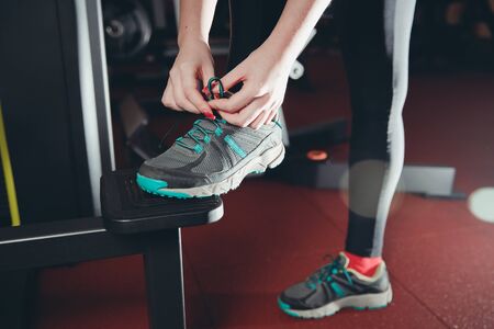 Close-up of girl tying shoelaces on sports shoes in gym.の写真素材