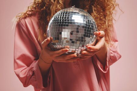 Close-up of disco ball is mirror, girl in pink dress with curly hair is holding ball for parties and dances. Concept holiday, birthdayの写真素材