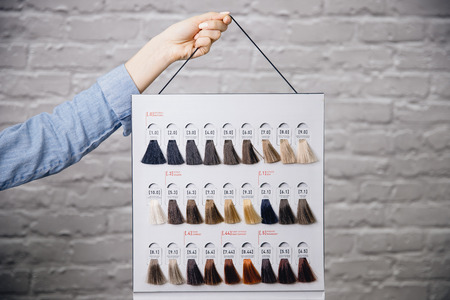 Hairdresser holds palm hair color palette against white brick wall. Hair coloring in salonの写真素材