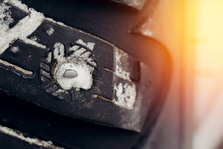 Winter tires. Close-up of iron insertion of thorns in rubber on background of snow and glare of...