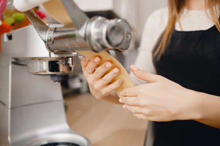 Girl is preparing dough noodle machine, cooking italian pasta, rolling the dough. Concept studio cooking food.の写真素材