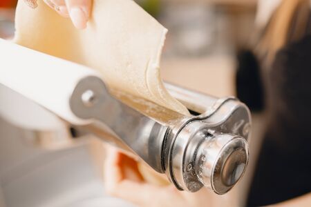 Girl is preparing dough noodle machine, cooking pasta, rolling the dough. Concept studio cooking food.の写真素材