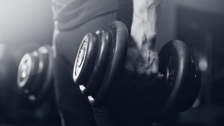 Dumbbell. Close-up of man lifts dumbbell to biceps in gym.