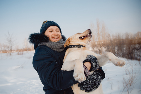 Selfie with the dog. A man plays with a labrador in winter, wearing a winter hat and a jacket. Concept of love and friendshipの写真素材