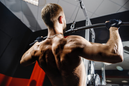 Man muscles are back. Close-up of an athlete makes traction on muscles of delta, shoulders, biceps