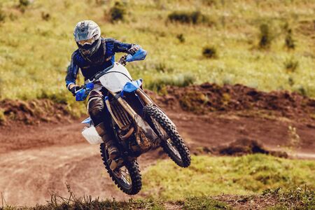 Racer on dirtbike motorcycle jumps and takes off over the track, in background opponent is catching up. Concept primacy, rivalry, competition, extremeの写真素材