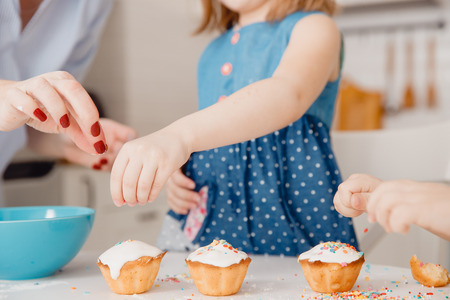 Children with their hands sprinkle cupcakes with colored caramel for Easter. Concept happy family.の写真素材