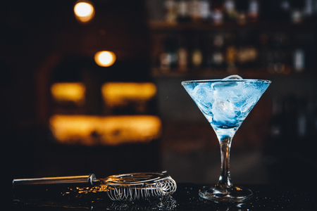 Close-up of blue martini cocktail glass is on bar. Dark background.の写真素材
