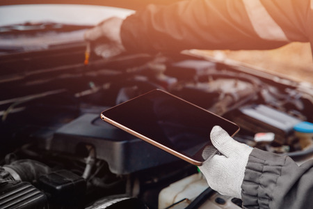Close-up of auto mechanic diagnoses car using tablet computer.の写真素材