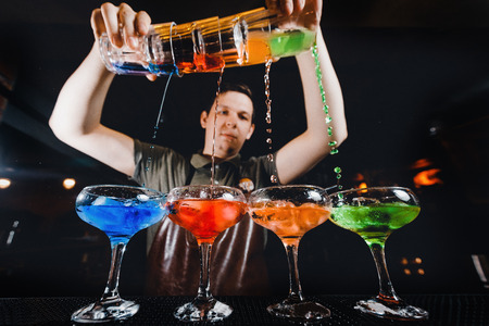 Barman mixes cocktail show with colorful alcoholic cocktails at bar counter.の写真素材