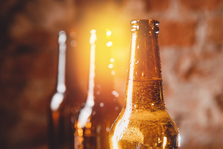 Row cold ice beer brown bottles glass with drops of water against brick wall. Concept craft breweryの写真素材