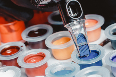 Close-up of tattoo machine collects pigment of different colors in boxes into needles.の写真素材