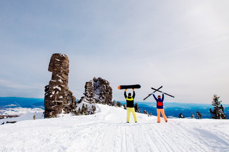 Two friends of young woman and man are holding skis and snowboards in background of snow mountains.の写真素材