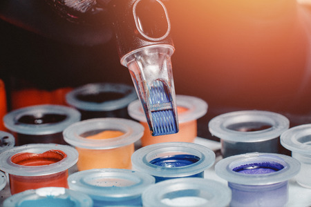 Close-up of tattoo machine collects pigment of different colors in boxes into needles.の写真素材