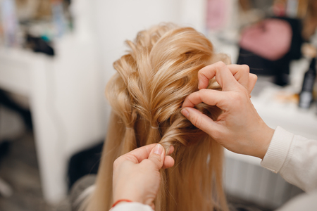 Woman hairdresser making hairstyle to blonde girl in beauty salon.の写真素材
