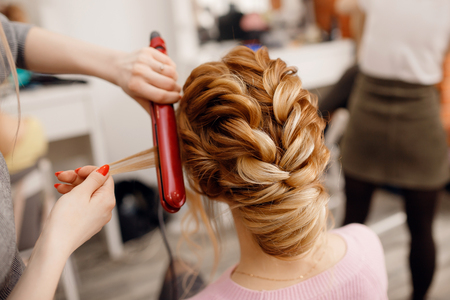 Woman hairdresser making hairstyle to blonde girl in beauty salon.の写真素材