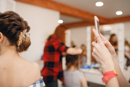 Hairdresser takes pictures of woman phone with finished hairstyle high beam on light backgroundの写真素材