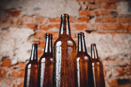Row cold ice beer brown bottles glass with drops of water against brick wallの写真素材