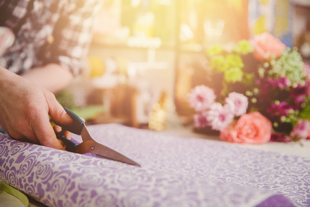 Man florist collects modern bouquet of roses, cuts scissors packaging for gift.の写真素材