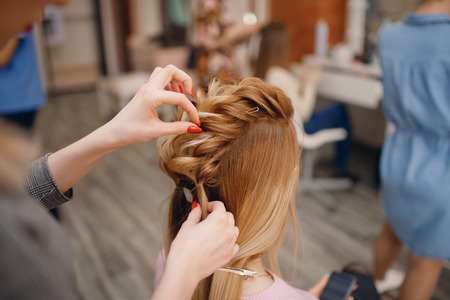 Hairdresser woman conducts training for pupil in salon, weaving braid hair, wedding styling.の写真素材