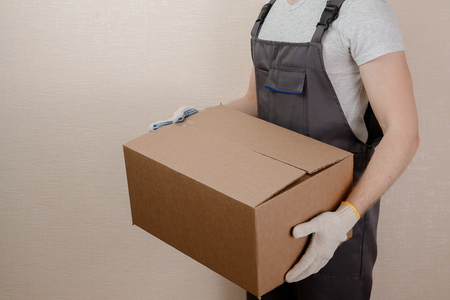 Man in uniform of delivery suit, loader, in hands of cardboard box for thingsの写真素材