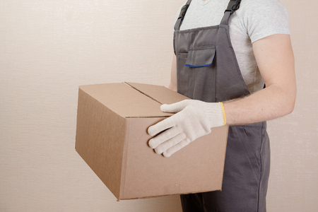 Man in uniform of delivery suit, loader, on his head white helmet, in hands box with loadの写真素材