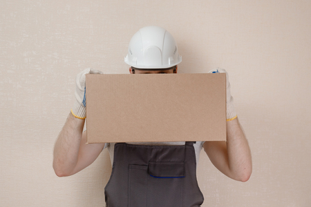 Man in uniform of delivery suit, loader, on his head white helmet, in hands box with loadの写真素材