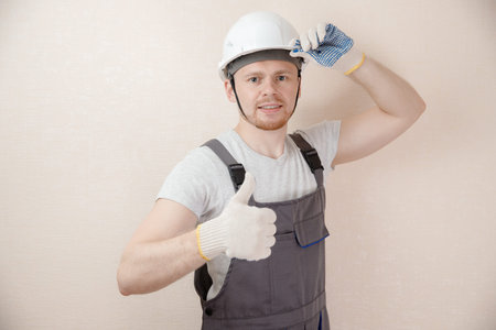 Man in to uniform of delivery suit, loader, on his head white helmet, shows gesture like, cool
