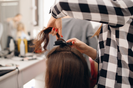 Hairdresser woman straightens her hair and makes styling, close-up of curling iron in salonの写真素材