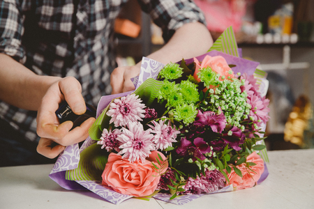 Man florist collects modern bouquet of roses, stapler fastens packaging.の写真素材
