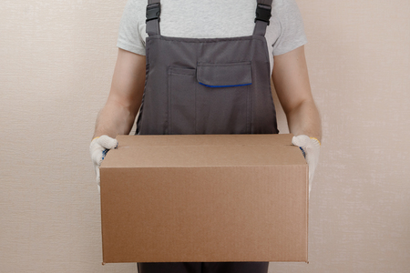 Man in uniform of delivery suit, loader, in hands of cardboard box for thingsの写真素材