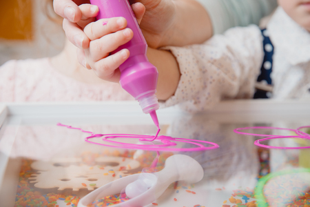 Close-up of baby man hand holds liquid paint in bottle of purple, drawings on table.の写真素材